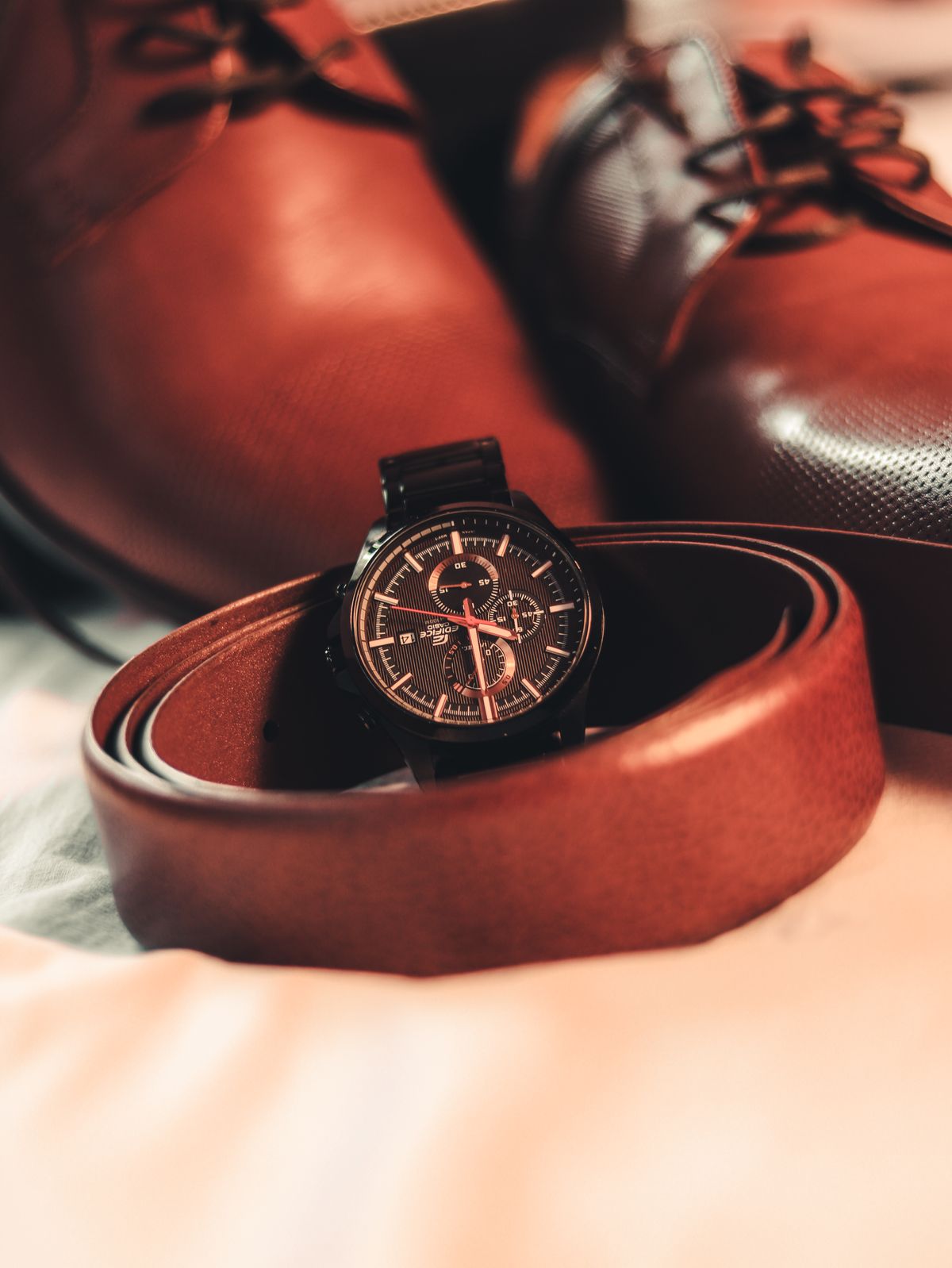 Brown leather shoes beside a coordinating brown belt and watch.