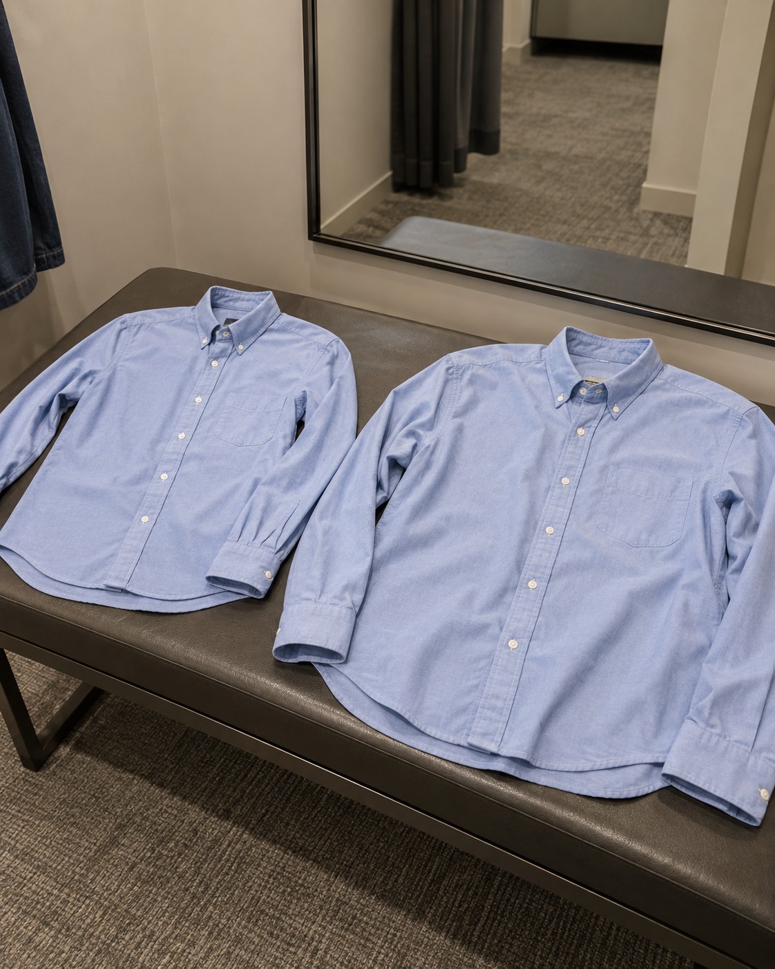 Two pale-blue shirts in different sizes on a fitting-room bench.