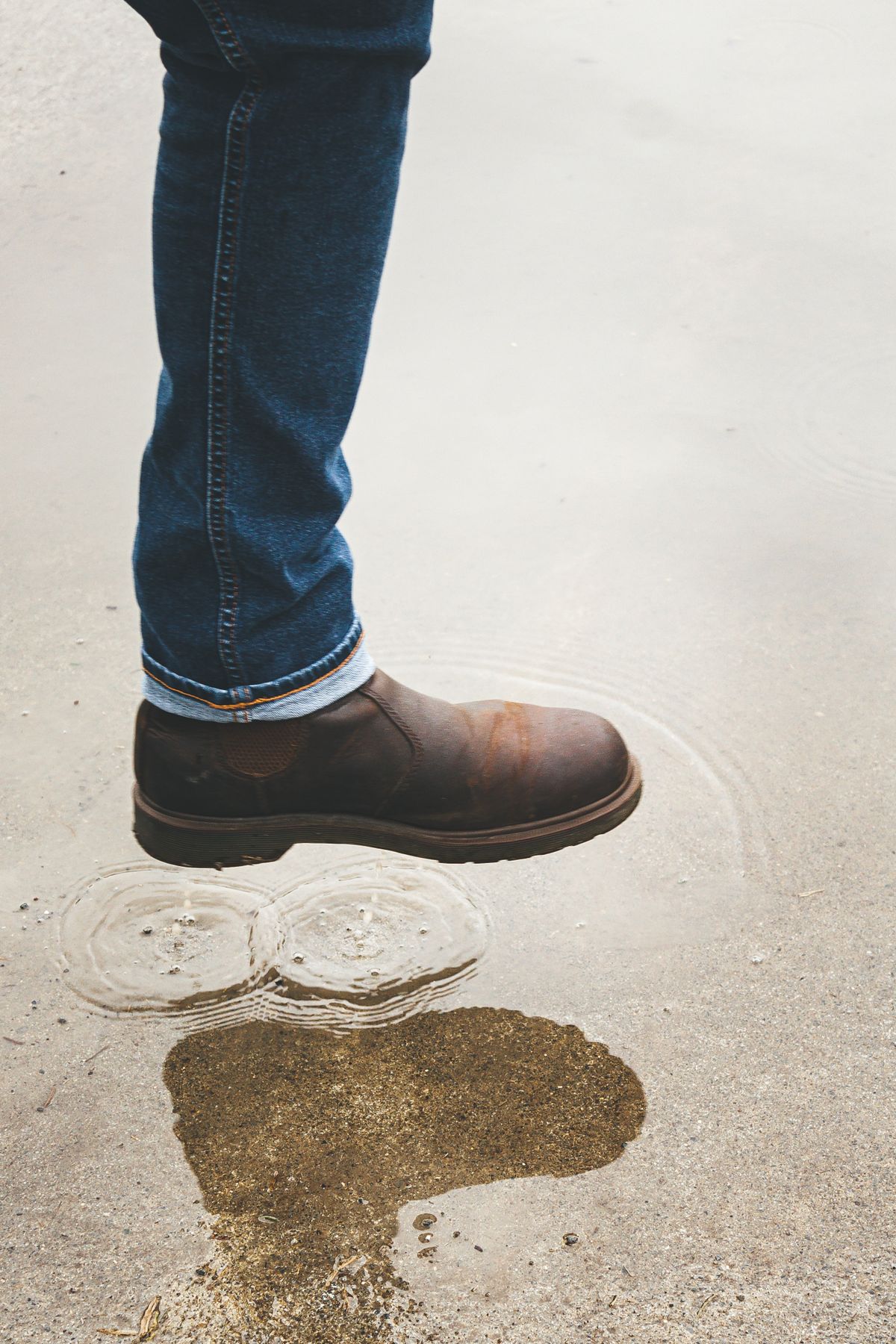 A brown leather Chelsea boot above wet pavement.