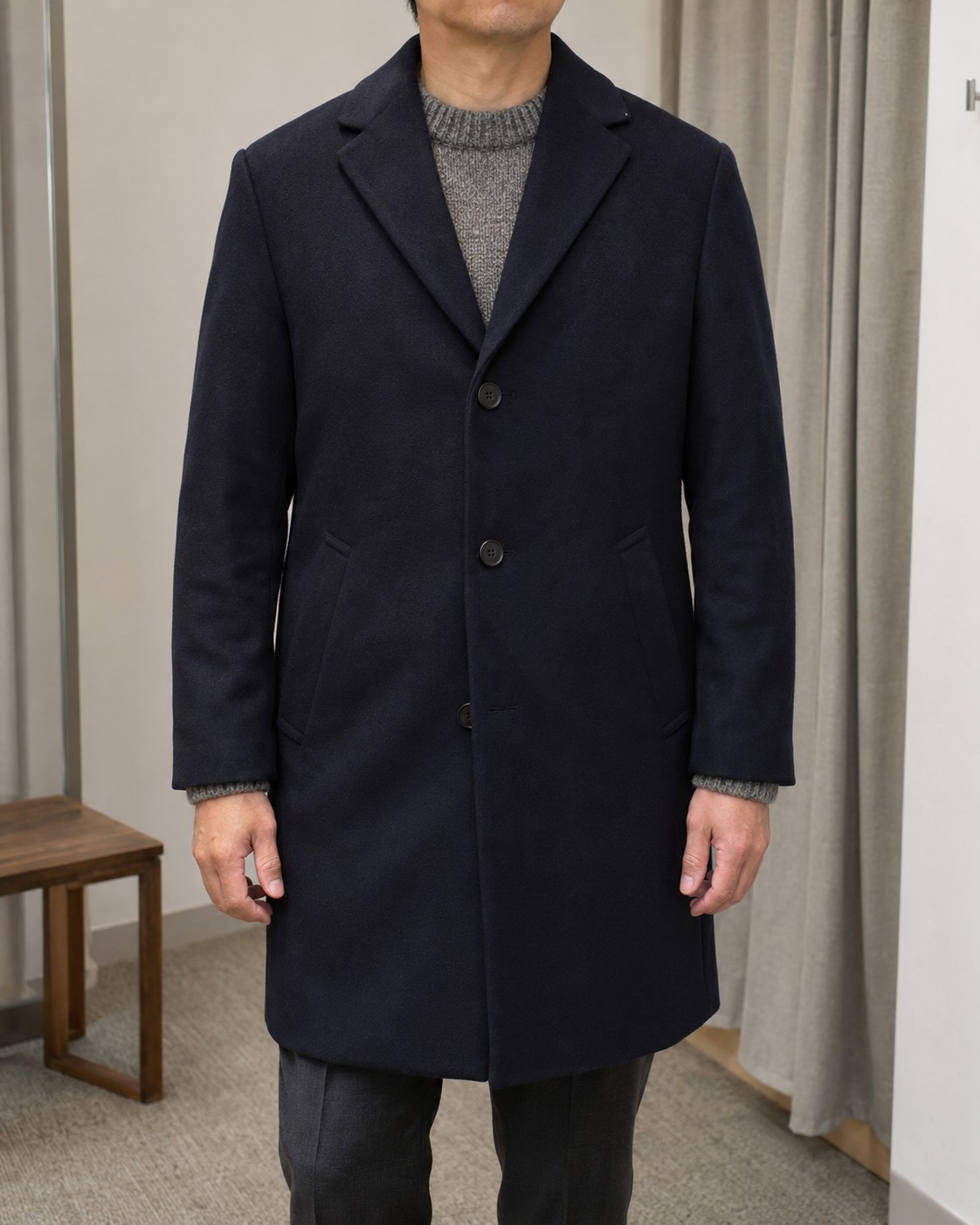 A navy overcoat fitted over a grey knitted jumper.