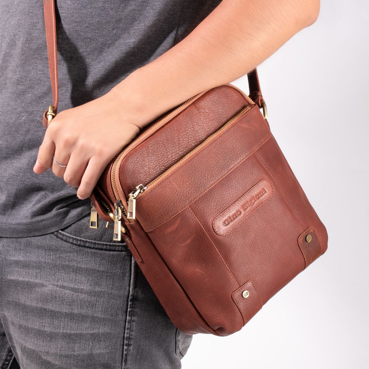 A brown crossbody bag worn over a grey top.