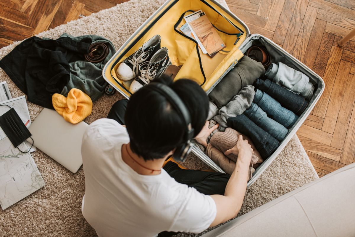 An overhead view of a man arranging folded clothes in a suitcase.