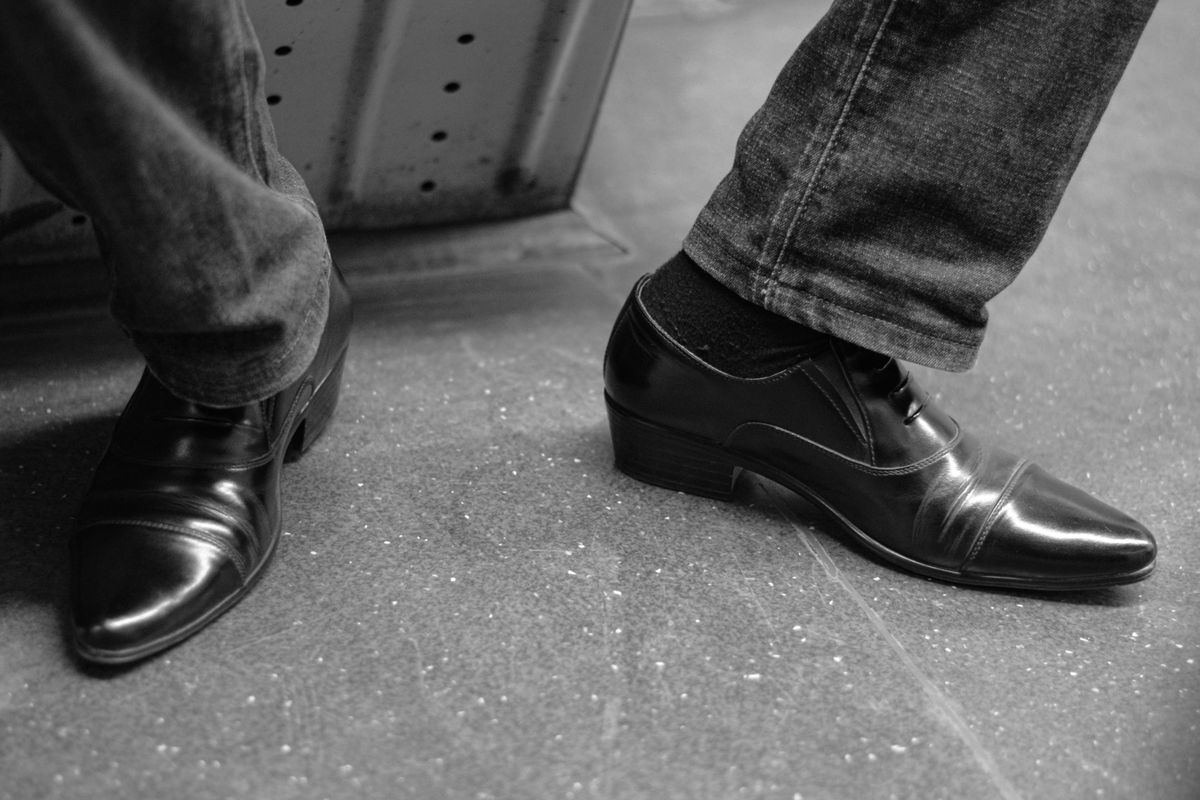 Black cap-toe Oxford shoes worn with grey trousers.