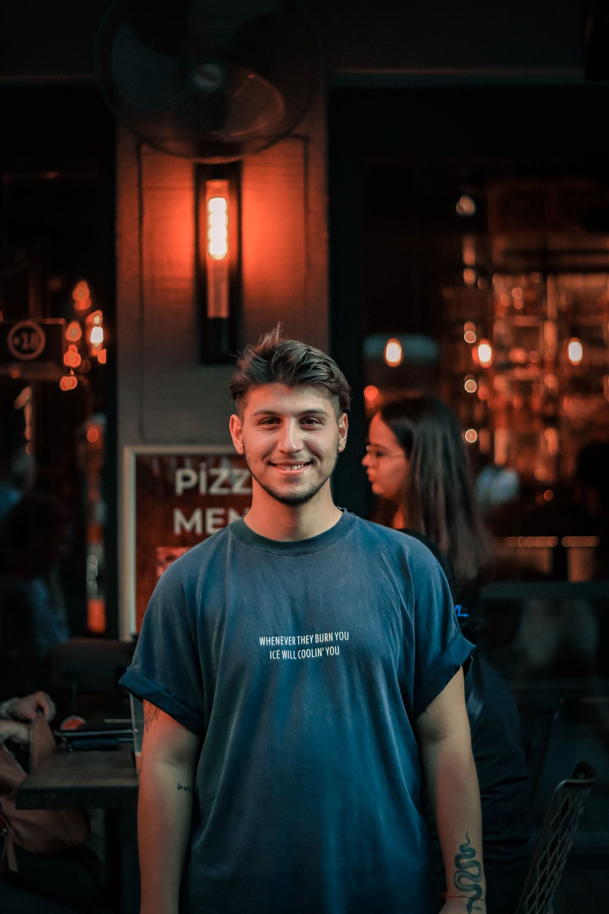 A man in a casual dark T-shirt outside a restaurant at night.
