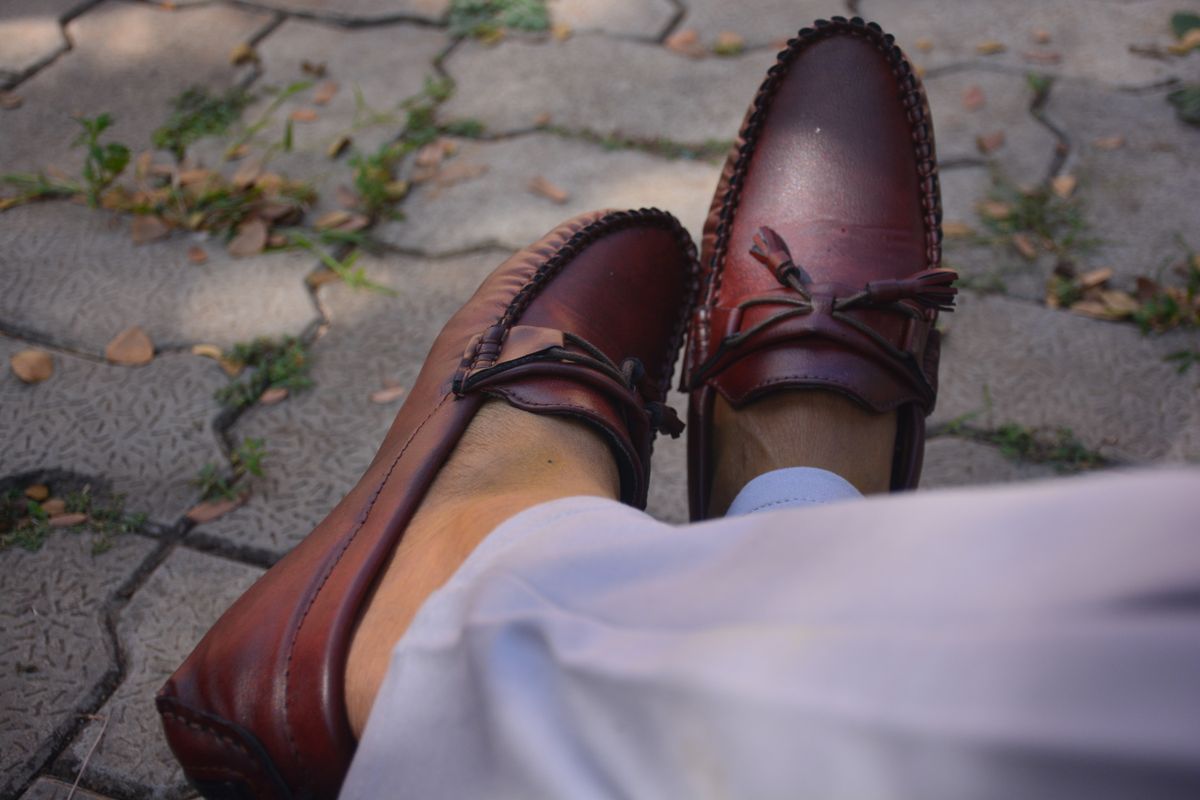 Burgundy loafers worn with light trousers on paving.