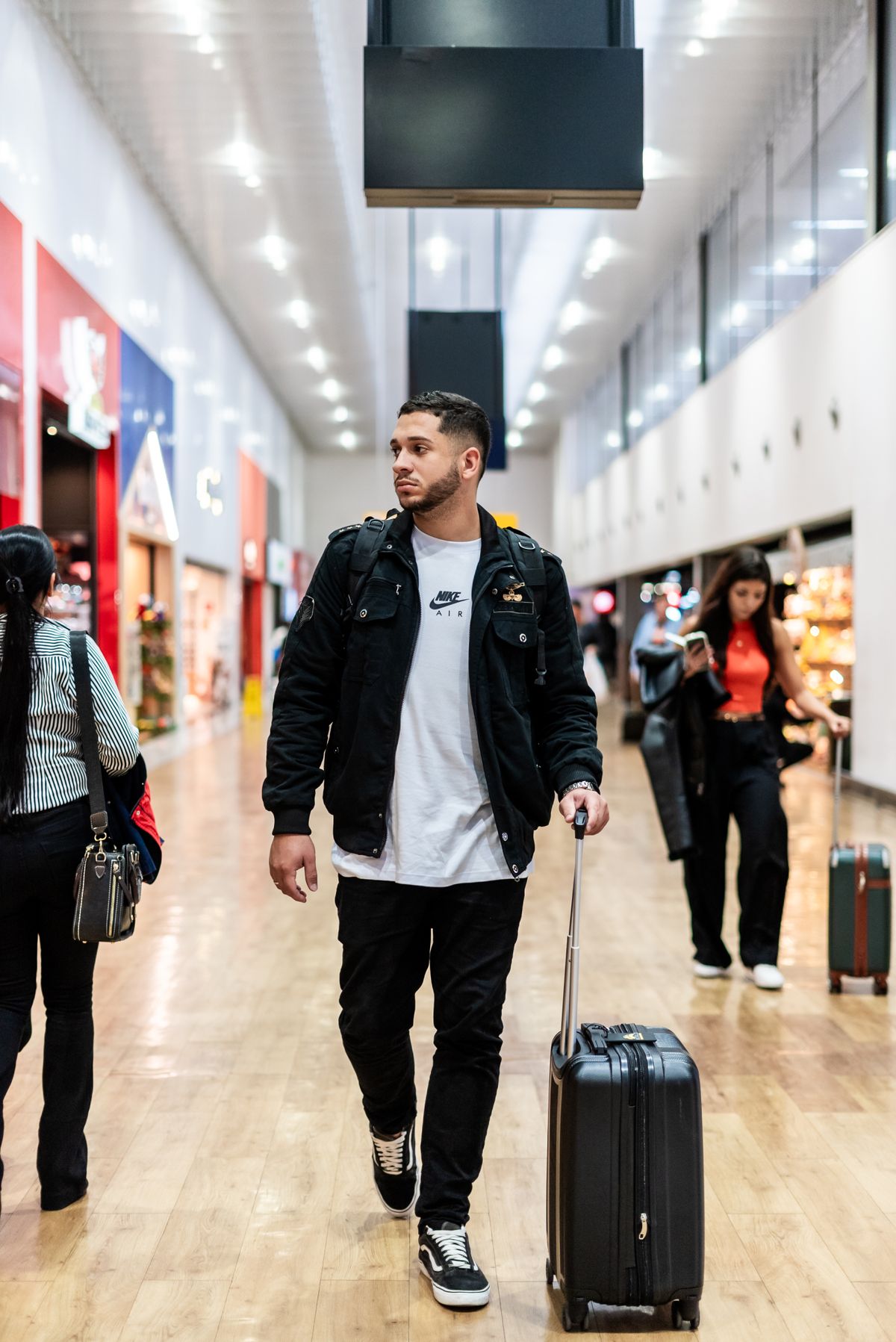 A traveller in layered casual clothing walking with a suitcase.