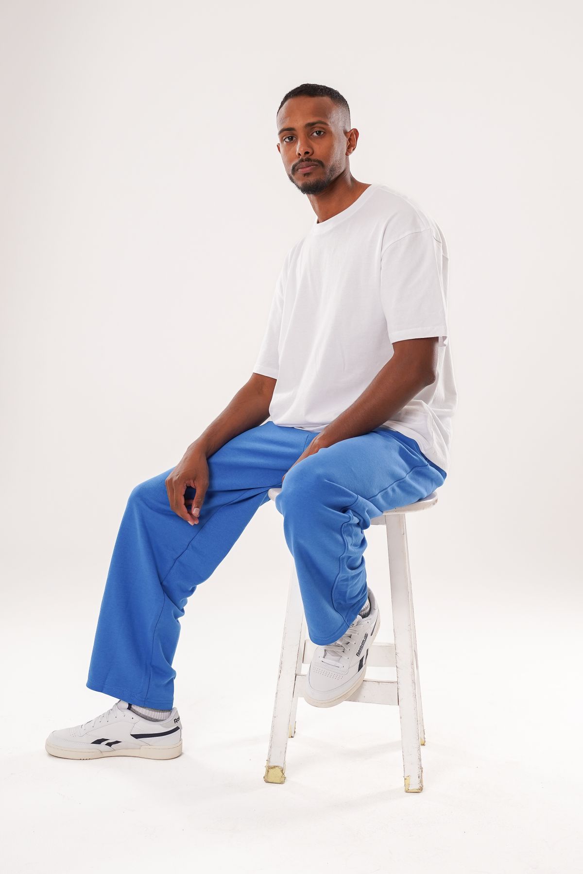 White trainers worn with blue trousers and a white T-shirt.