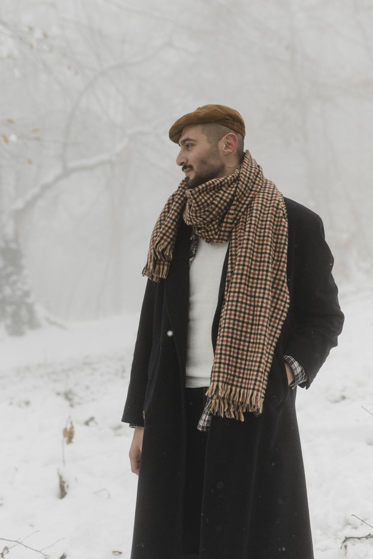 A man wearing a dark overcoat and textured scarf in snow.